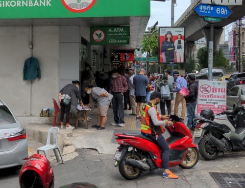 A lottery customer examines the numbers on offer. The lottery seller is next to.a bank, a very auspicious message in the Thai lottery.culture.